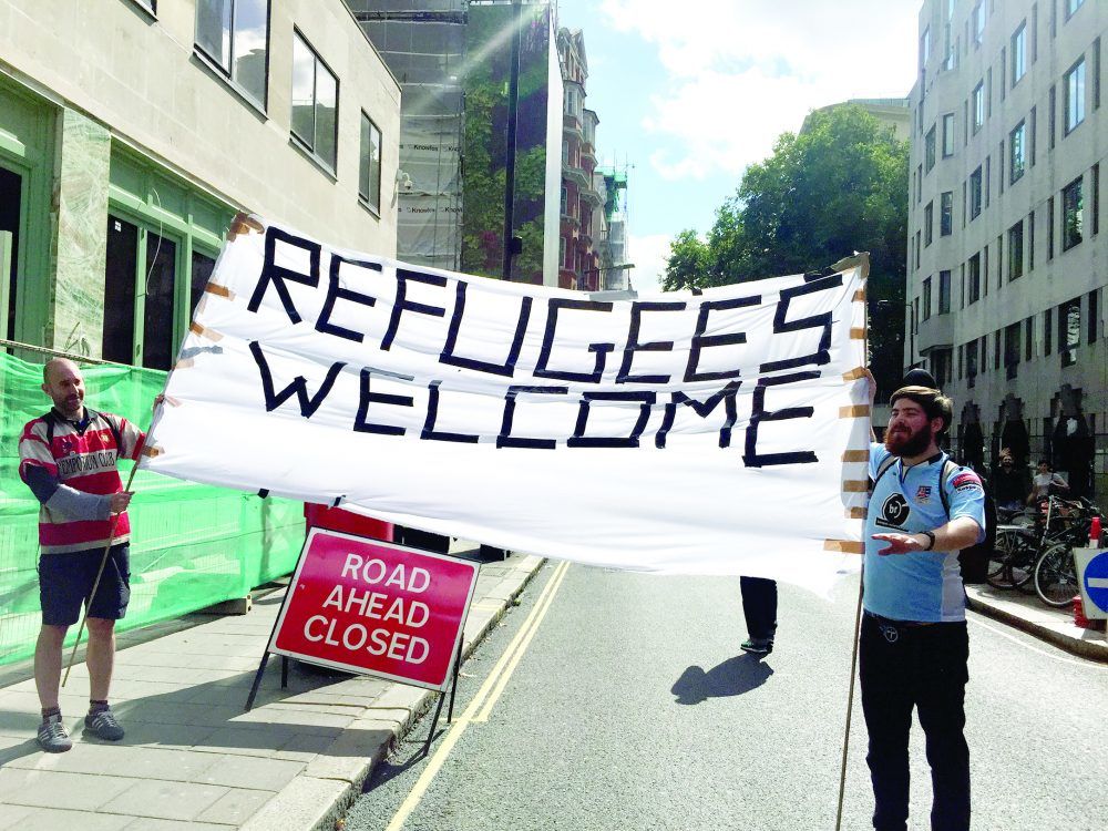 Jamie Cutteridge displays a banner with the slogan 'refugees welcome'