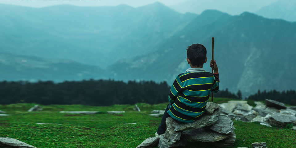 A boy sat on a rock with a staff
