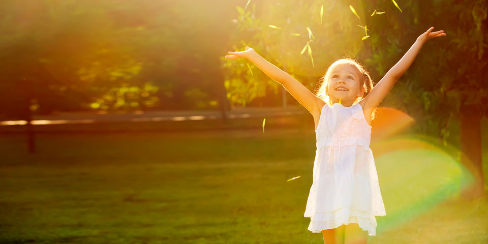 little girl standing in a green field with her arms in the air after throwing grass