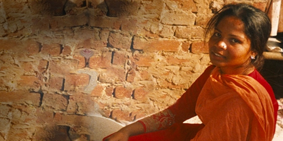 Asia Bibi sat in a small room with brick walls, smiling at the camera