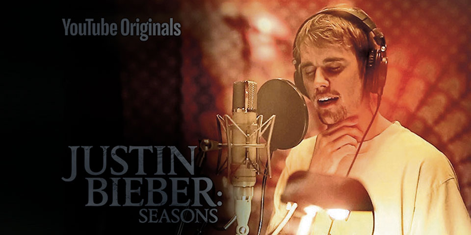 Justin Bieber singing into a recording mic with his eyes shut and a pair of headphones on