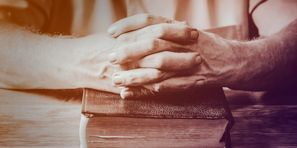 a man's hands with interlocked fingers, resting on top of a bible