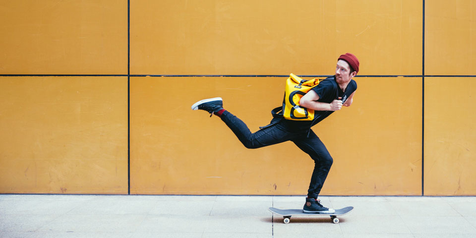 Young man on a skateboard looking back over his shoulder and leaning forwards as he skates from left to right