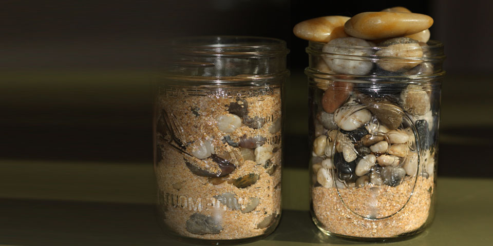 two glass jars side by side, filled with sand, pebbles and rocks