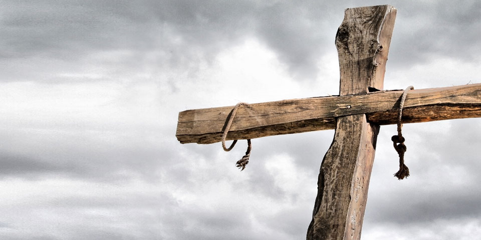 an empty cross pictured against a clouded grey sky